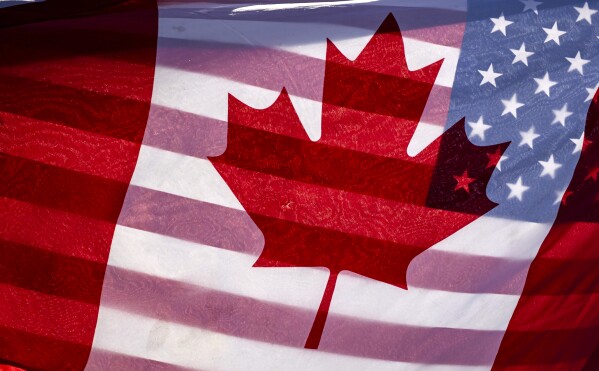 Sunlight shines through the flags of Canada and the United States, held together by a protester outside on Parliament Hill in Ottawa, Feb. 1, 2025.(Justin Tang/The Canadian Press via AP, File)